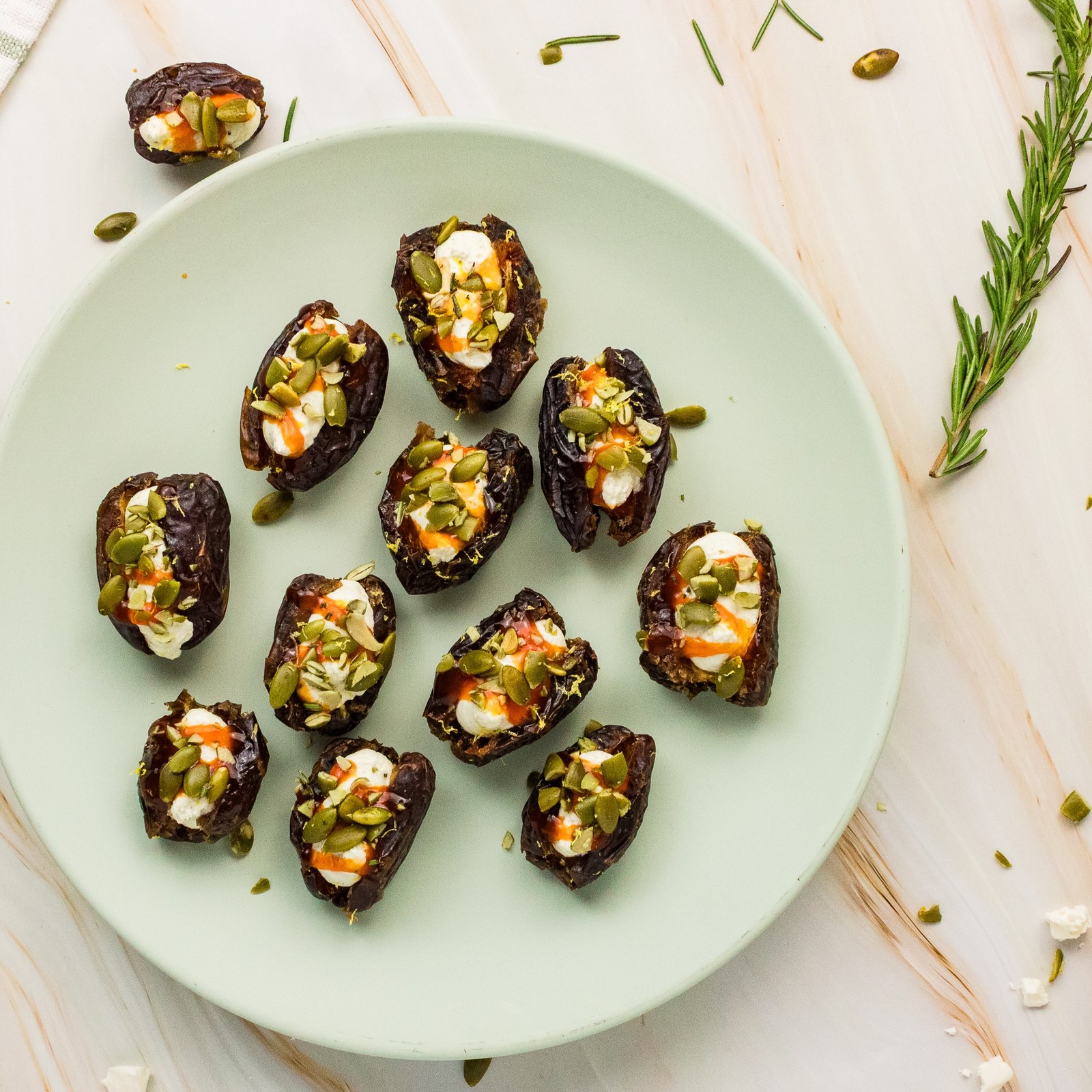 Overhead view of whipped feta stuffed dates with hot honey and pumpkin seeds on a pale green plate