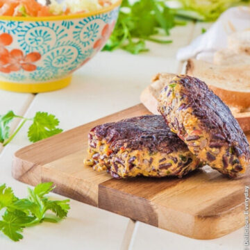Thai pumpkin black rice burgers stacked on a wooden cutting board