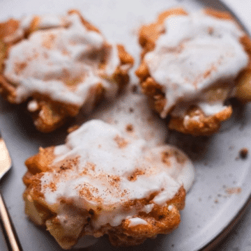 Three glazed vegan apple fritters dusted with cinnamon on a gray plate