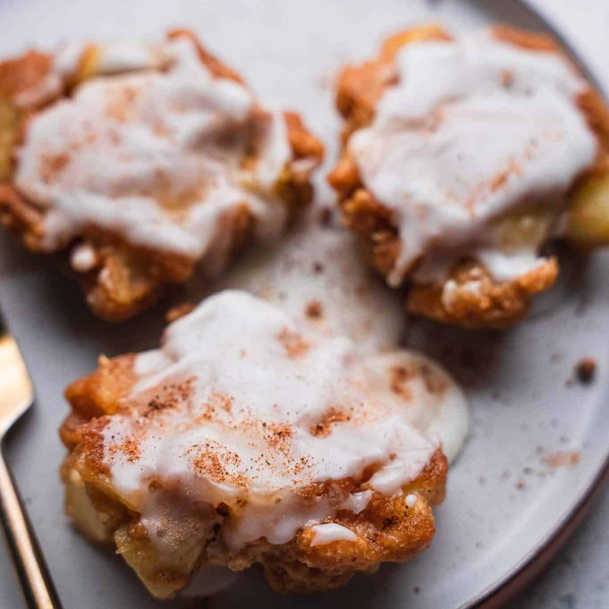 Three glazed vegan apple fritters dusted with cinnamon on a gray plate
