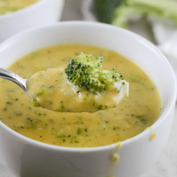 Vegan broccoli cheddar cheese soup in a white bowl with a spoonful lifted out