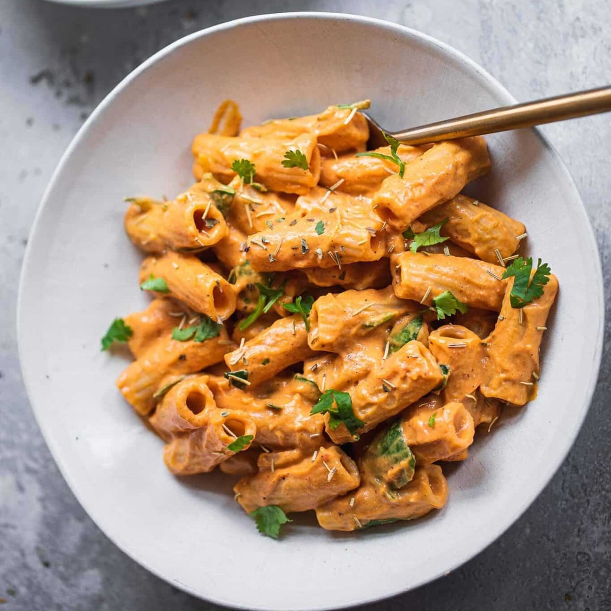 Bowl of creamy vegan butternut squash pasta with rigatoni, spinach and fresh herbs