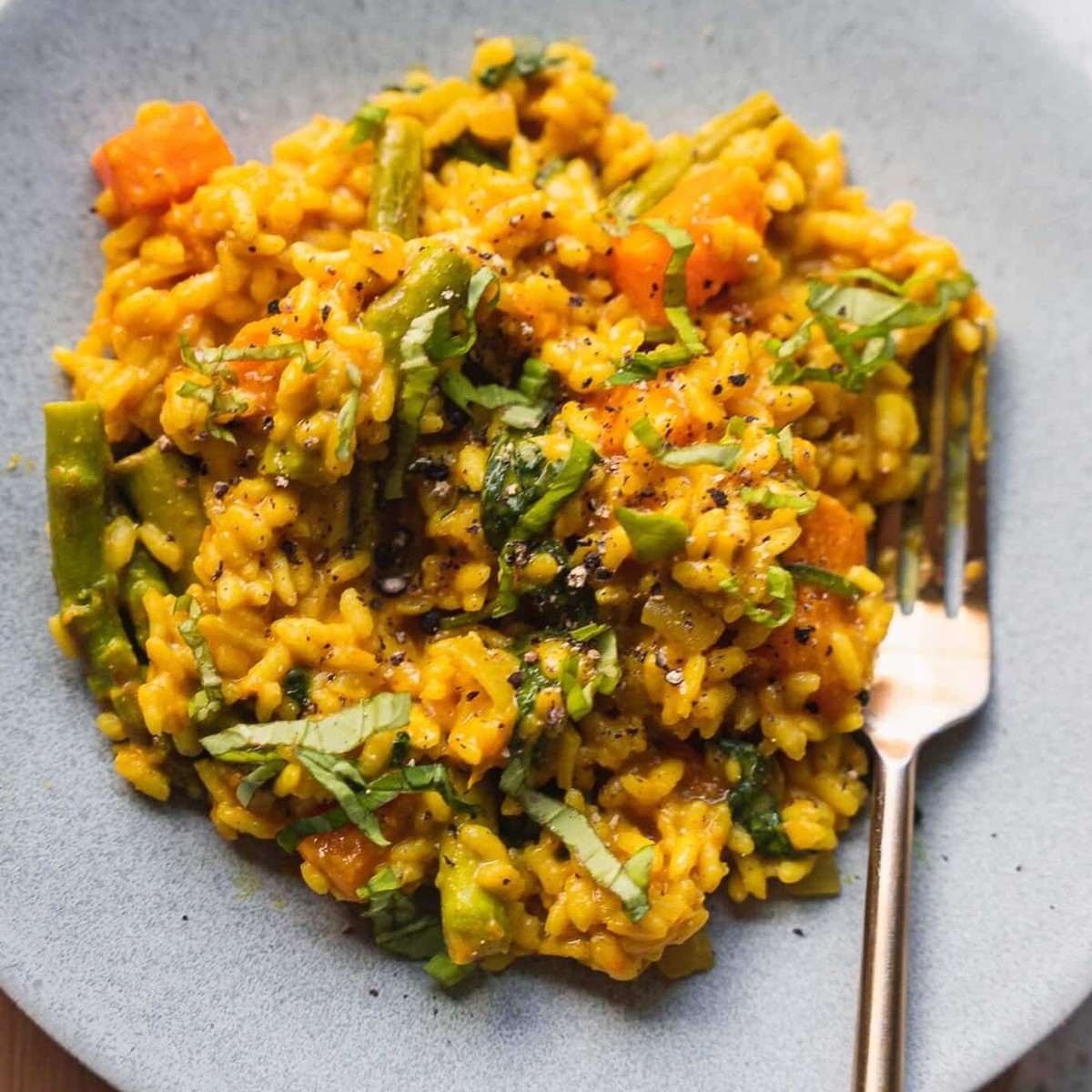 Vegan butternut squash risotto with asparagus, spinach and basil on a grey plate with a gold fork
