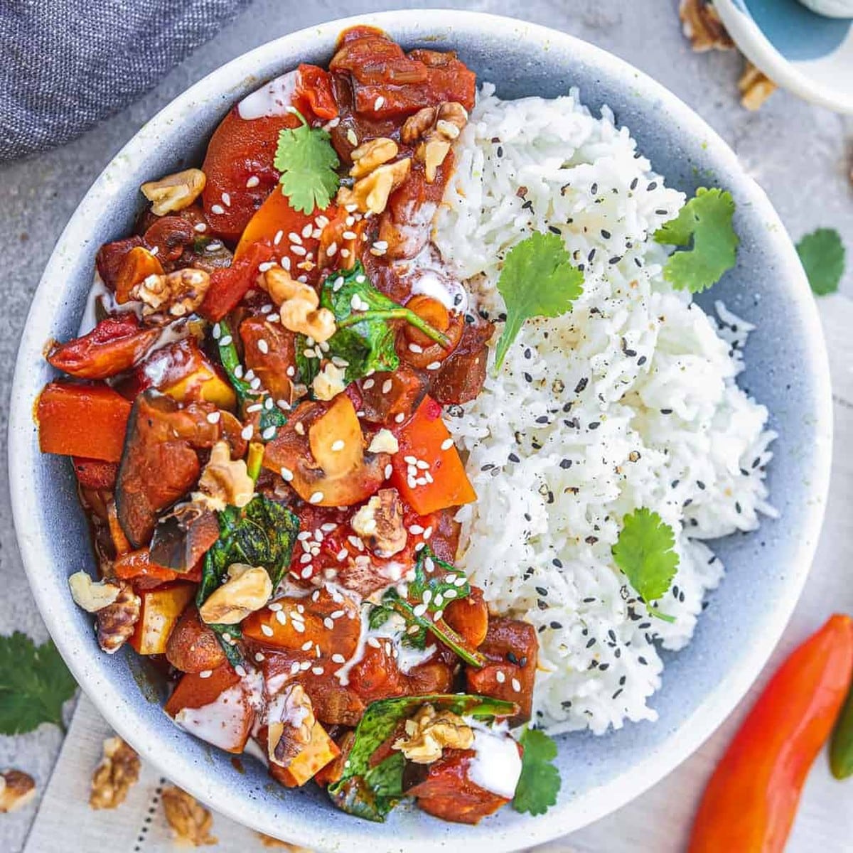 Vegan eggplant butternut squash curry with white rice, cilantro and walnuts in a blue bowl