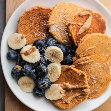 Vegan pumpkin pancakes on a white plate with blueberries, sliced banana and almond butter