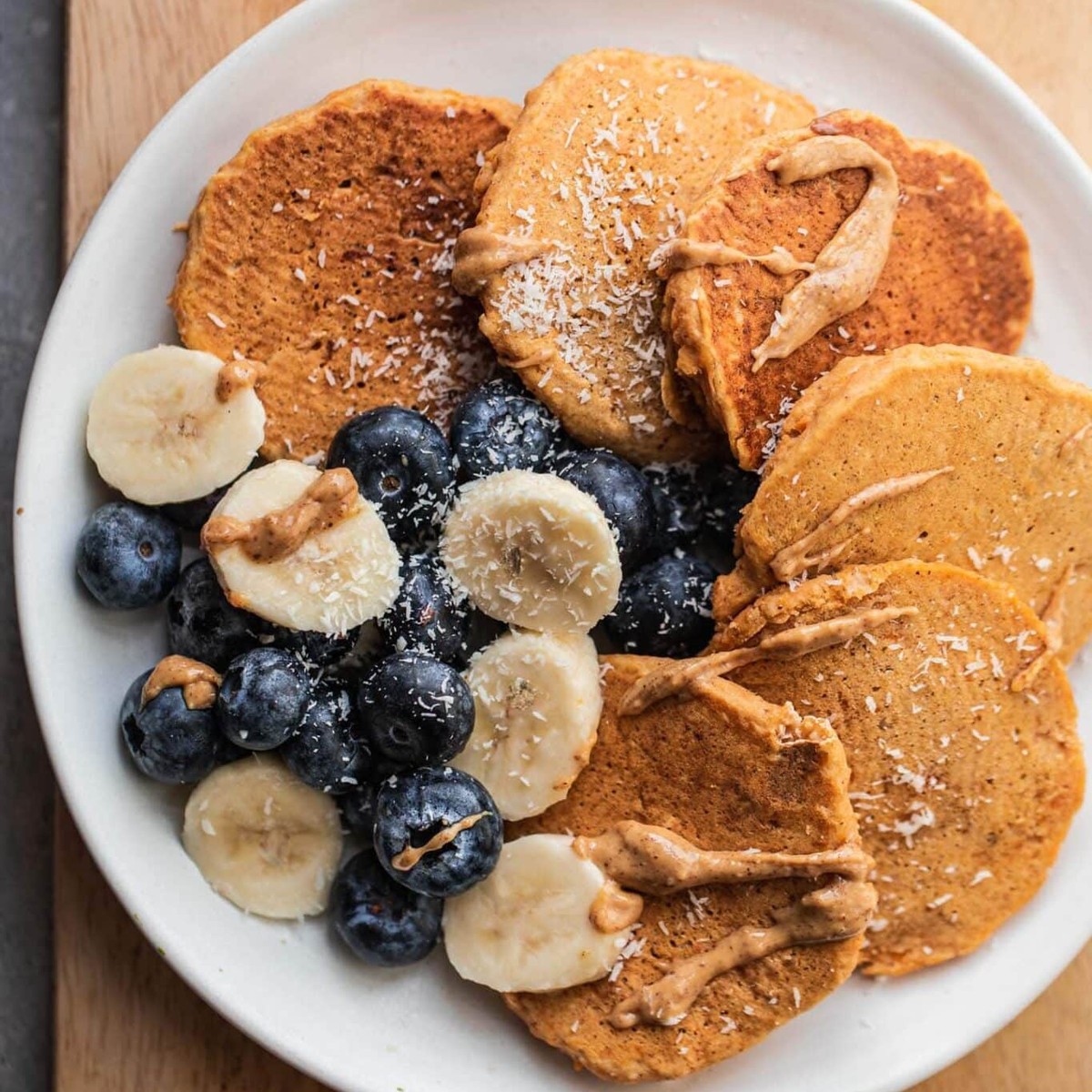 Overhead view of gluten-free vegan pumpkin pancakes with blueberries, banana and almond butter drizzle