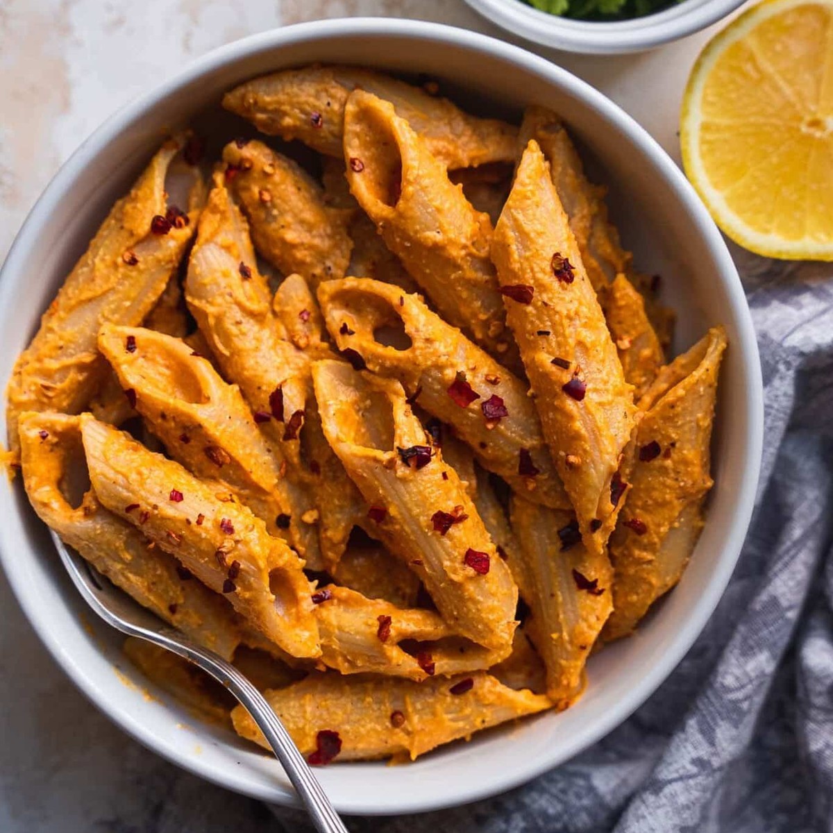 White bowl of creamy vegan pumpkin pasta with chili flakes, lemon and cilantro
