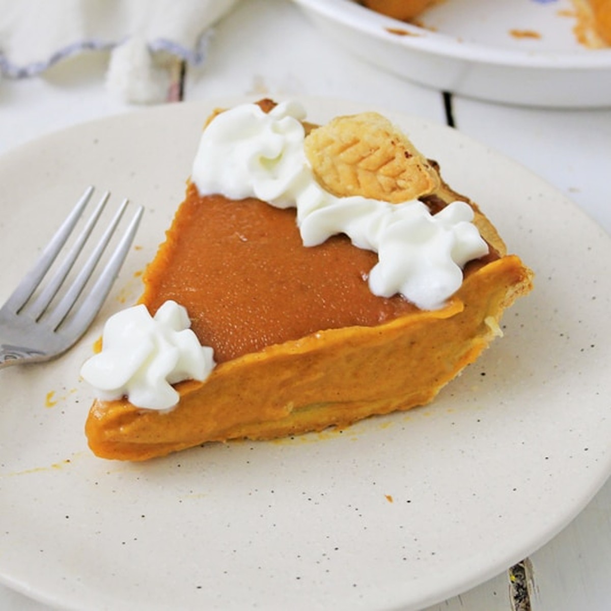 Slice of vegan pumpkin pie topped with coconut whipped cream on a white plate with a fork