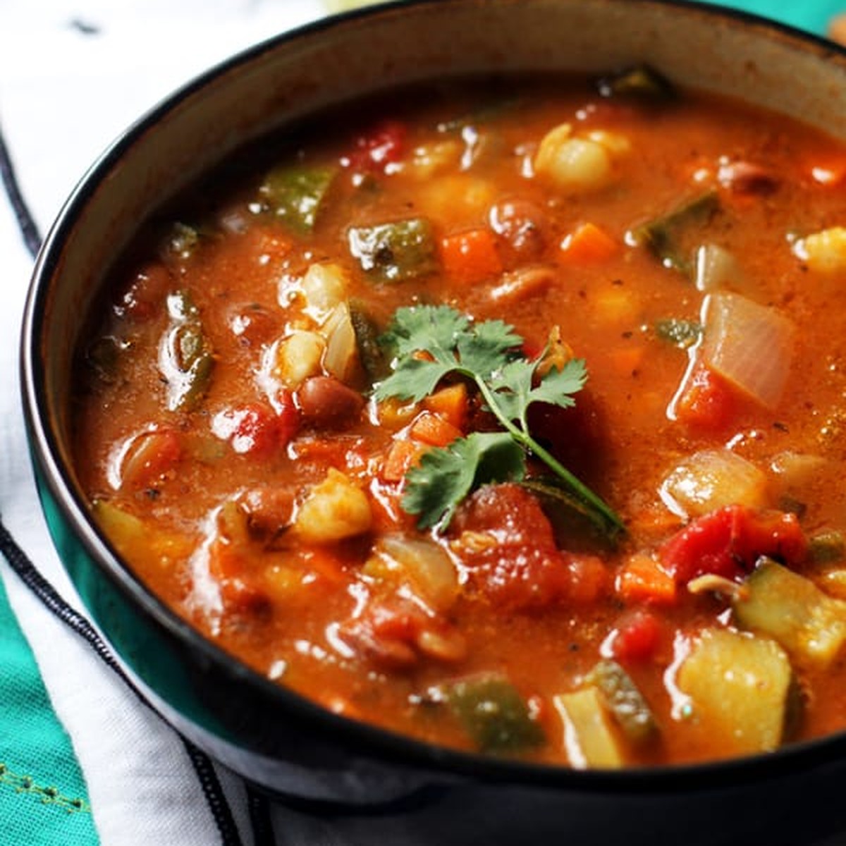 Close-up of vegetarian posole with hominy, pinto beans, poblano peppers and a cilantro sprig in a black bowl