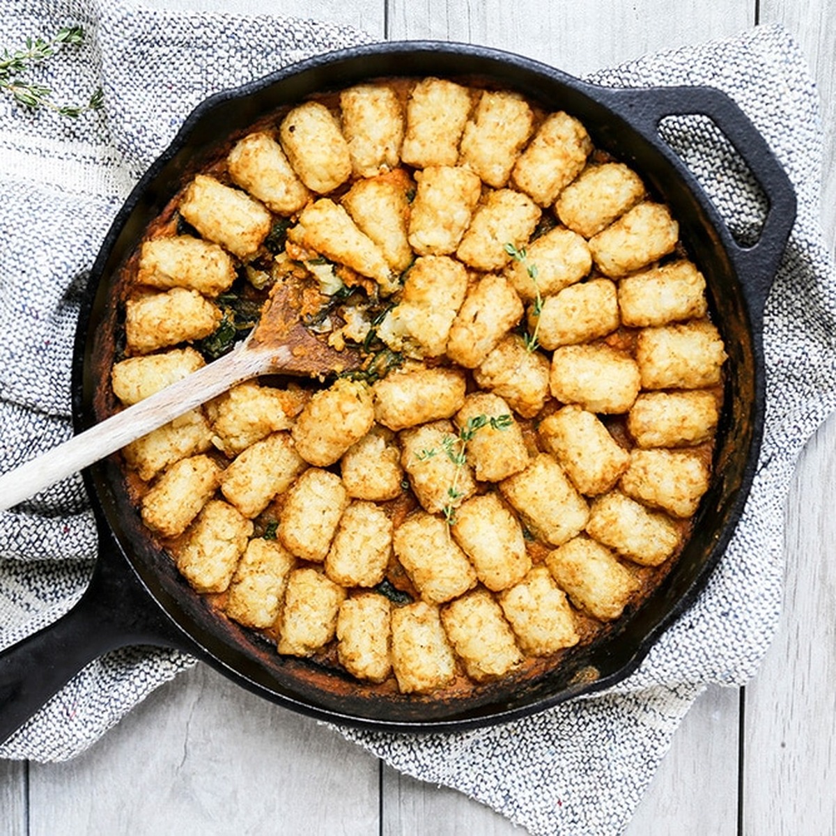 Vegetarian tater tot casserole with pumpkin, mushrooms and spinach in a cast iron skillet with a wooden spoon