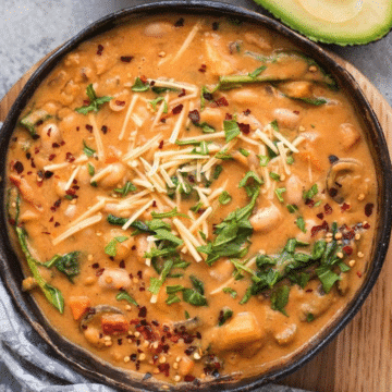 Vegetarian white bean chili in a dark bowl topped with spinach, vegan cheese and chili flakes