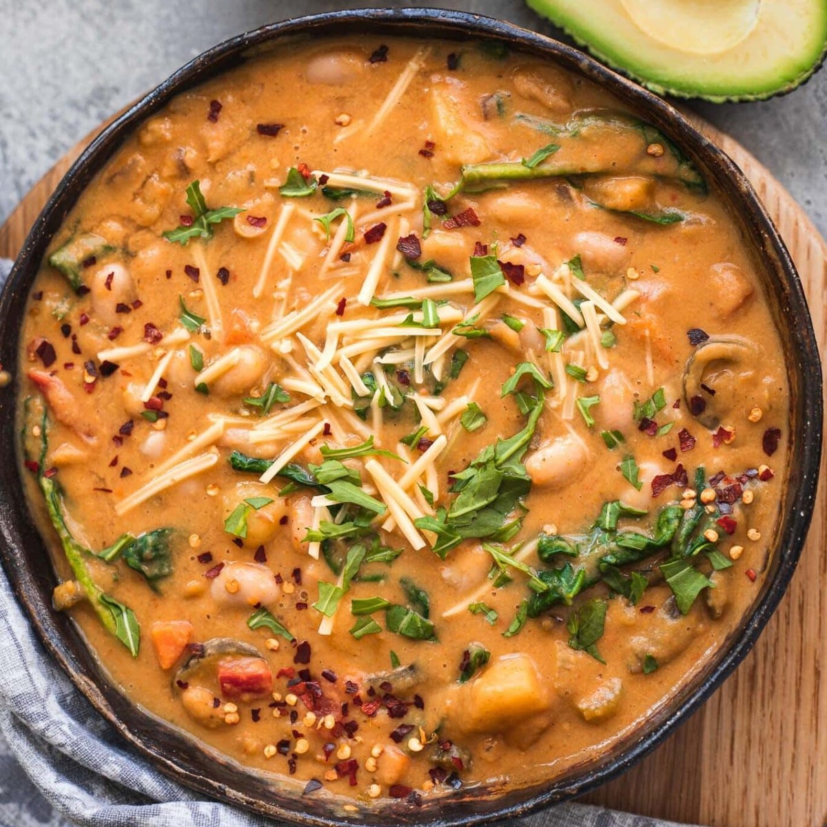 Bowl of vegetarian white bean chili with potatoes, spinach, vegan cheese and chili flakes